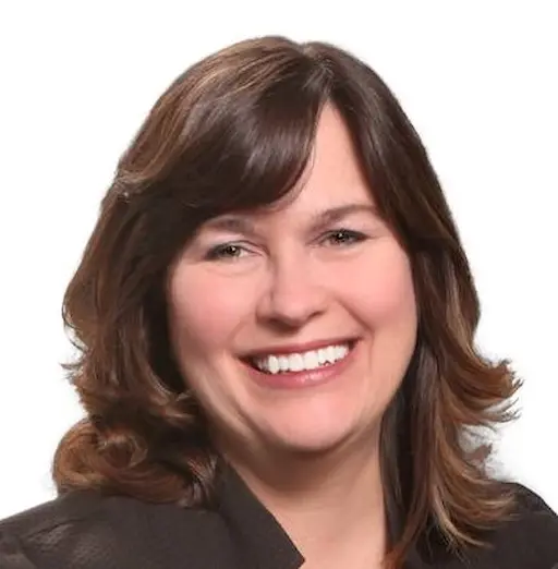 A smiling woman with shoulder-length brown hair, wearing a dark blazer, against a plain white background.